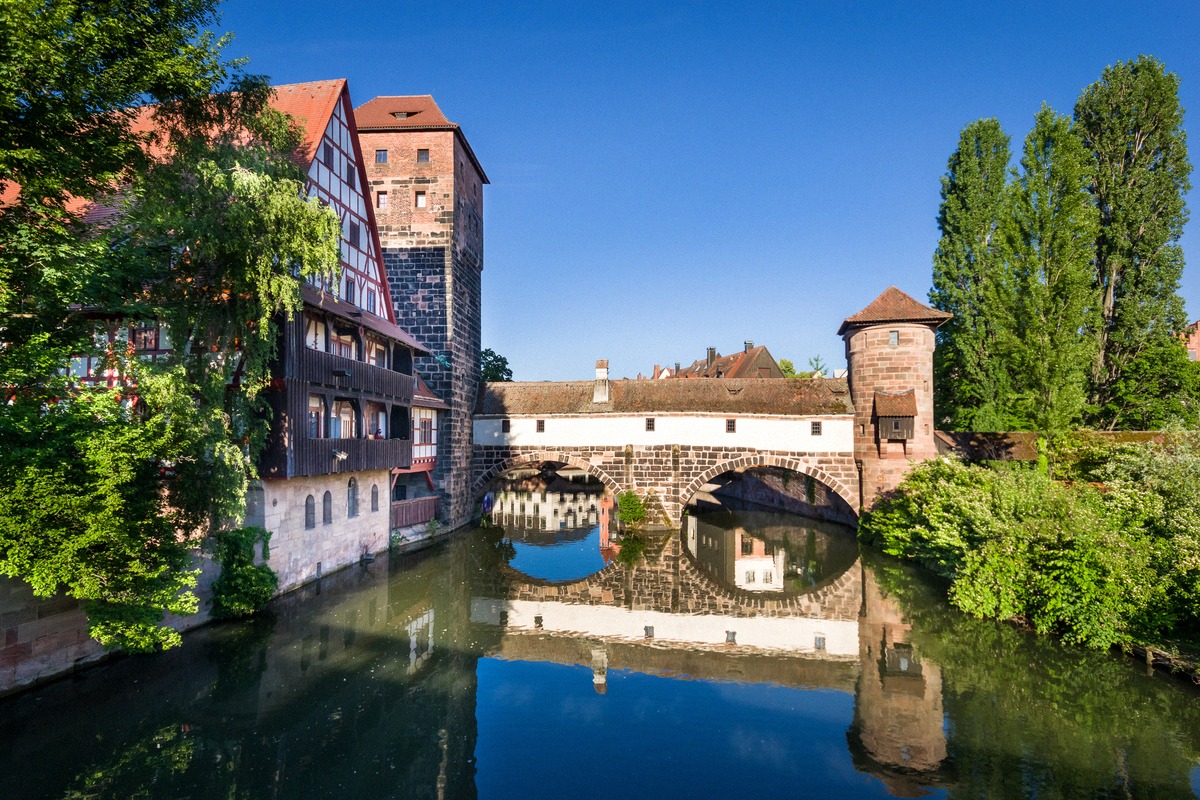 Die historische Maxbrücke über die Pegnitz mit dem mittelalterlichen Weinstadel und dem Wasserturm spiegeln sich im ruhigen Wasser